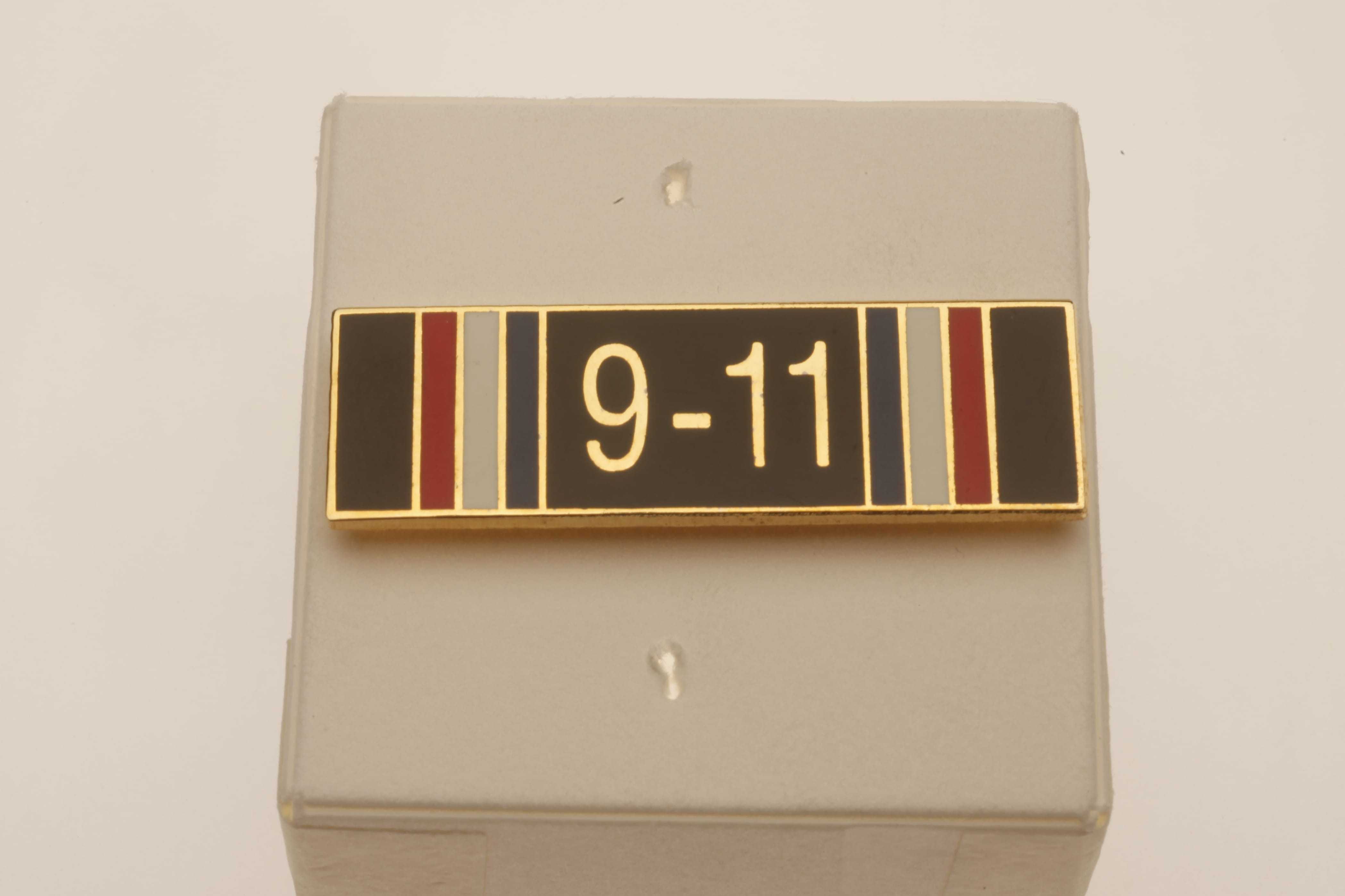 A rectangular pin with red, white, and blue stripes and "9-11" written in the center